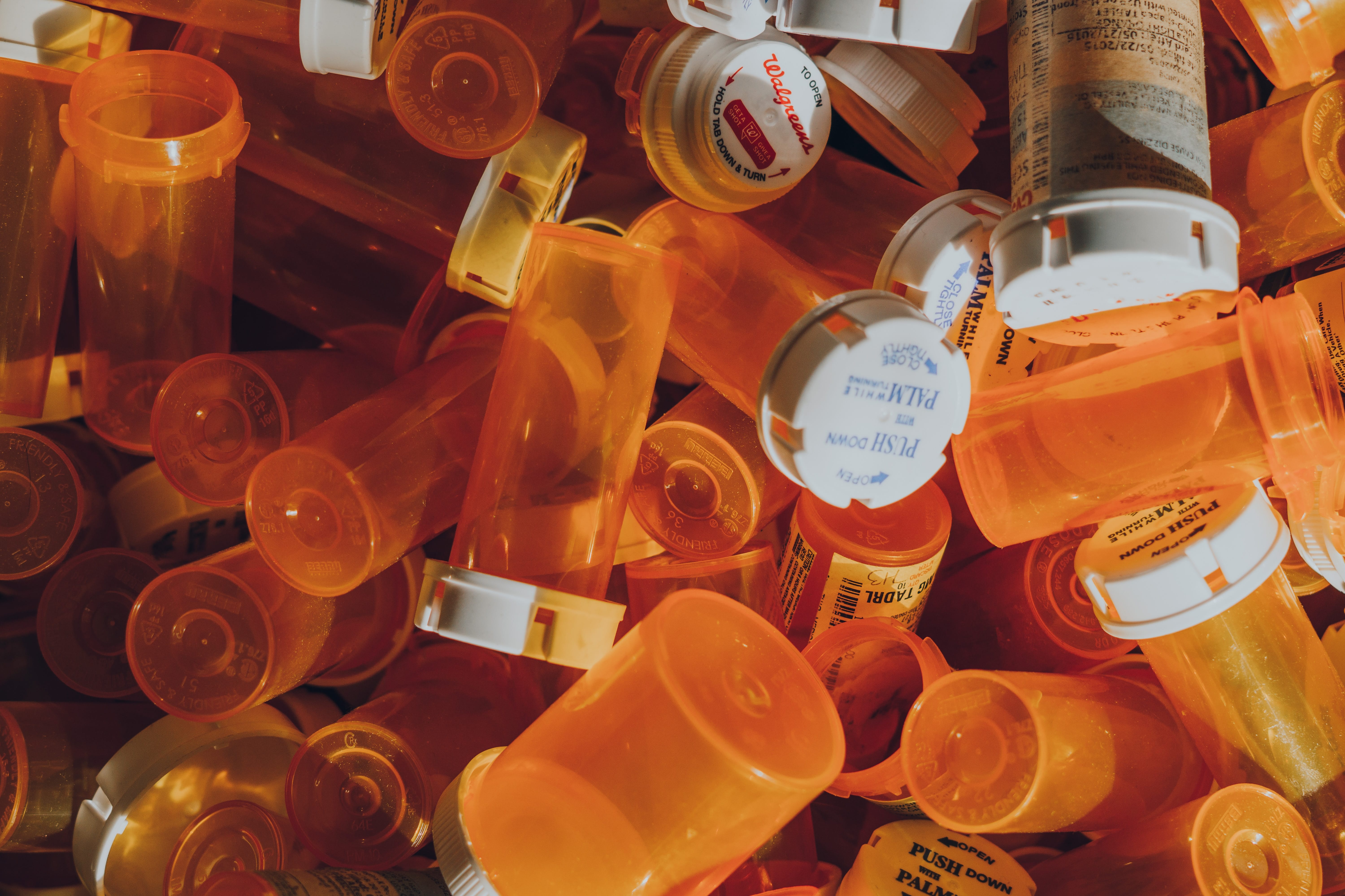 A pile of empty orange prescription bottles; image by Haley Lawrence, via unsplash.com.