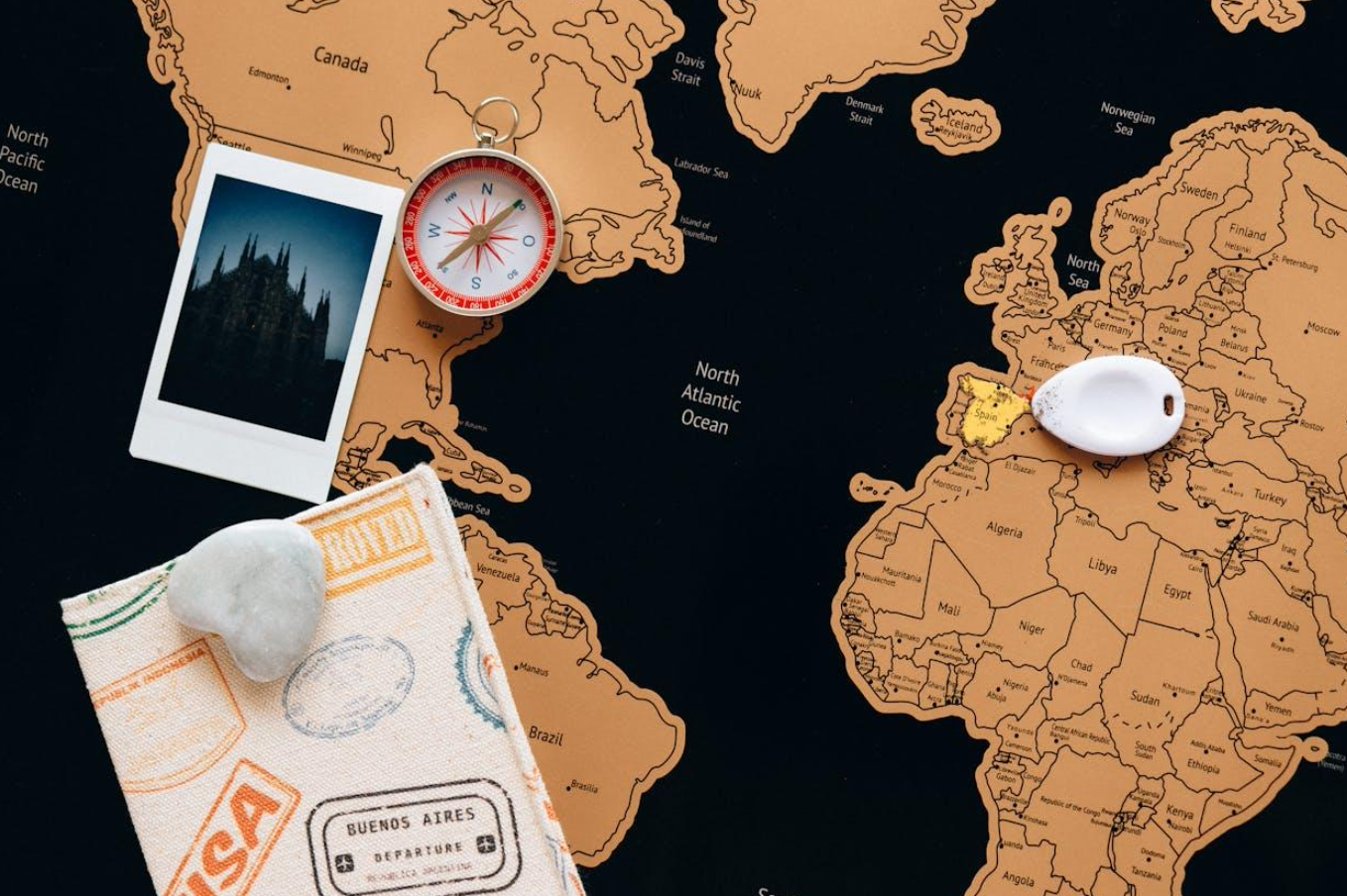 Map of the world with travel items laying on it; image by Nataliya Vaitkevich, via Pexels.com.