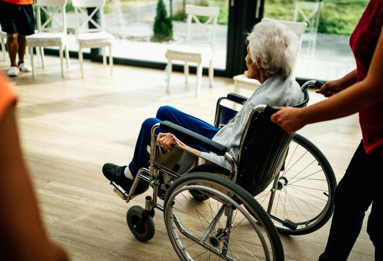 Elderly woman in wheelchair being pushed by female aide; image by Jsme MILA, via Pexels.com.