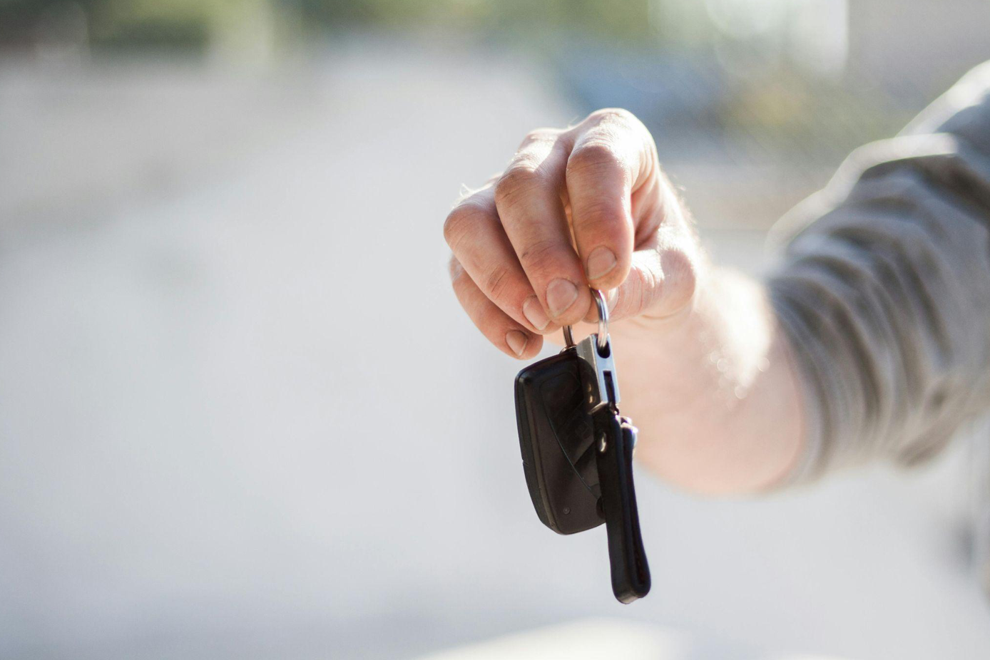 Man in grey shirt holding out car keys; image by Negative Space, via Pexels.com.