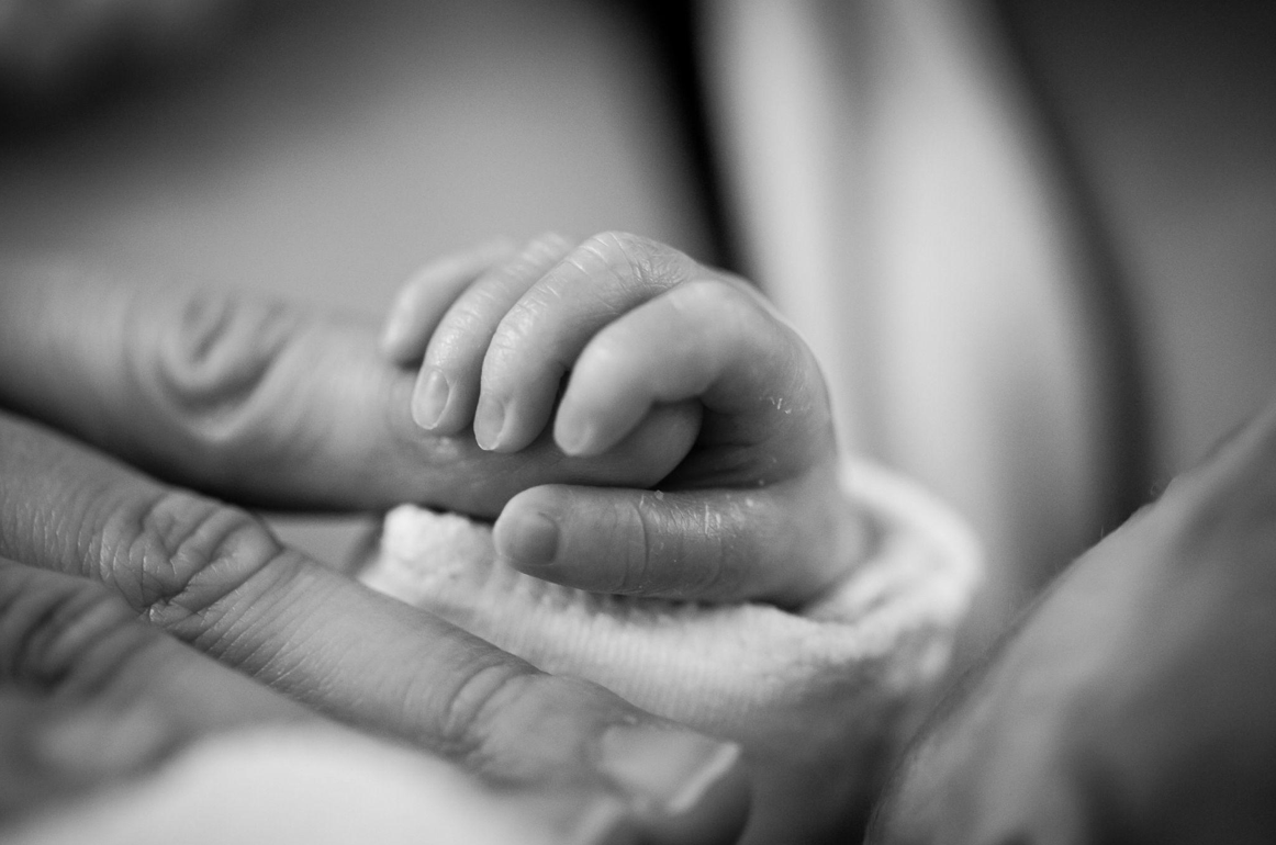 Grayscale shot of baby holding adult finger; image by Pixabay, via Pexels.com.