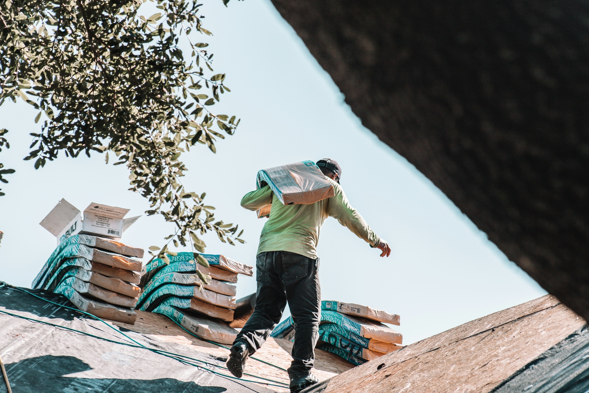 Roofer carrying shingles on roof; image by Zohair Mirza, via Unsplash.com.