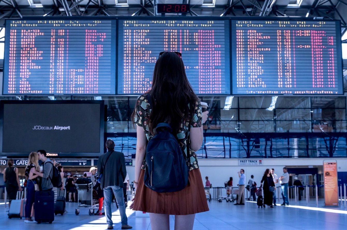 Woman reading flight arrival departure board at airport; image by JESHOOTS.com, via Pixabay.com.