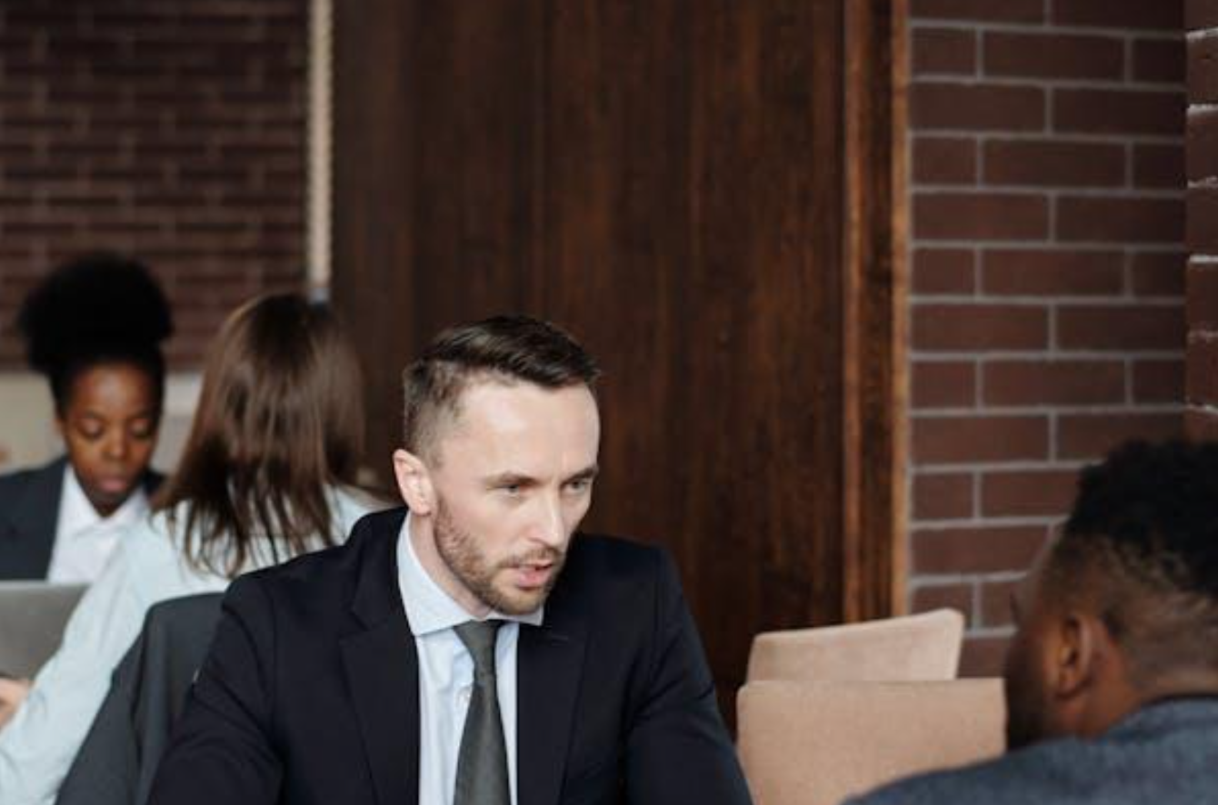 Businessmen talking at a cafe; image by August de Richelieu, via Pexels.com.