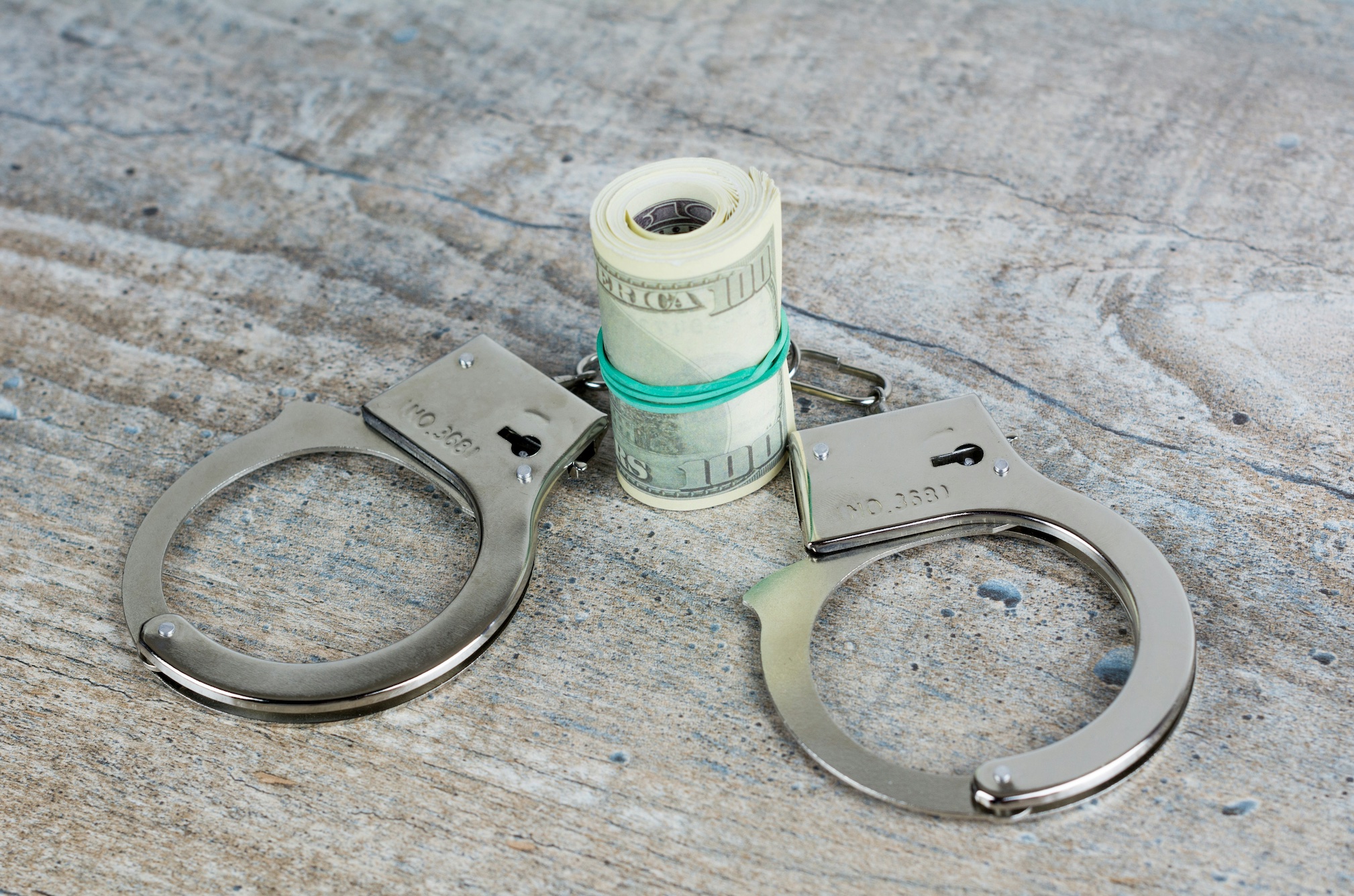 Handcuffs and US dollar banknotes on wooden background; image by Bermix Studio, via Unsplash.com.