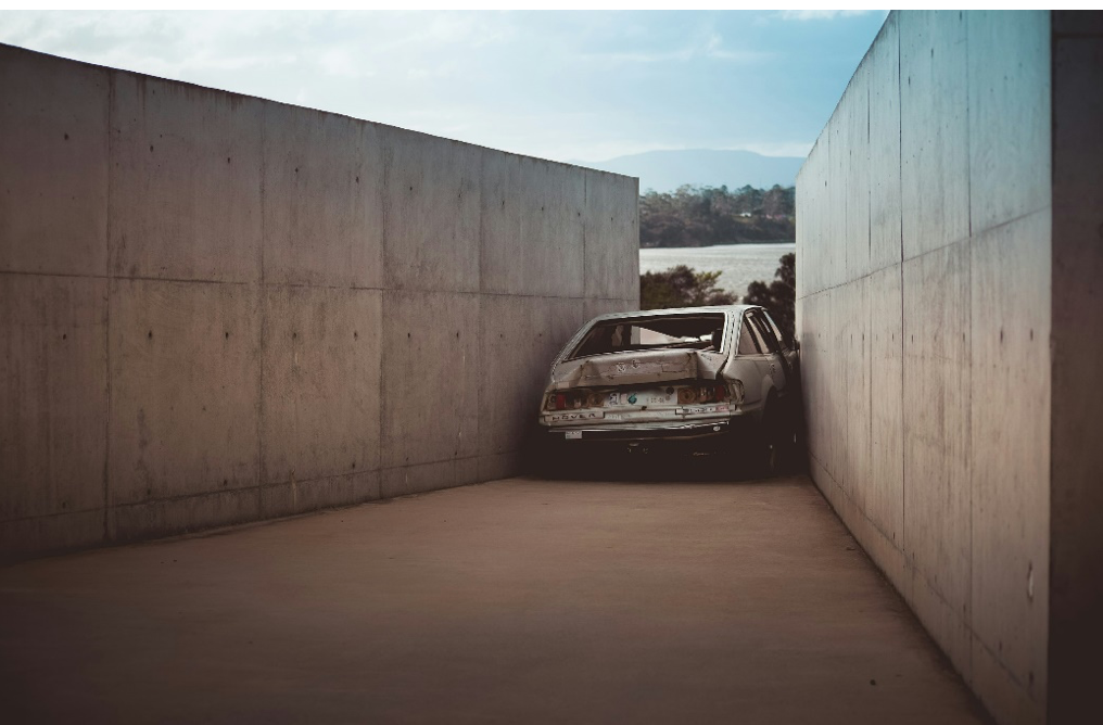 MONA Museum, Tasmania, wrecked gray vehicle between concrete walls at daytime; image by Gareth Harrison, via Unsplash.com.