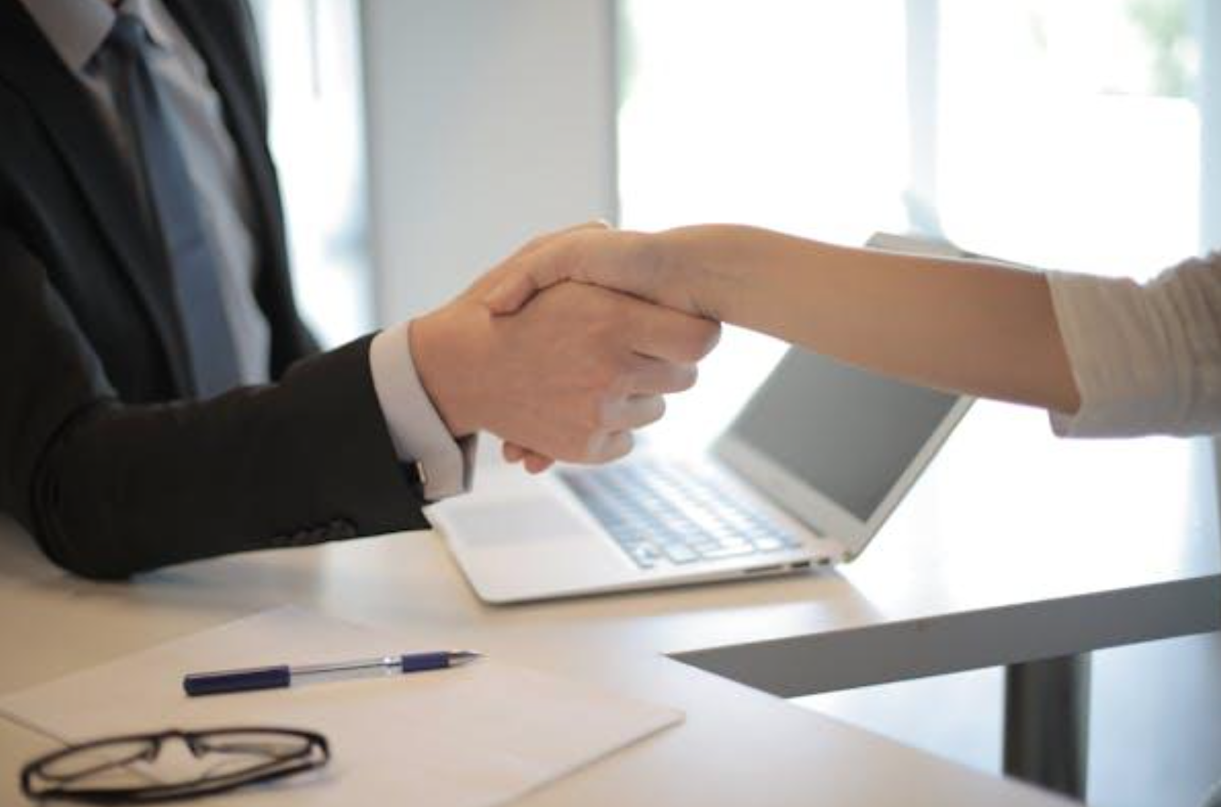 Man and woman shaking hands across desk; image by Andrea Piacquadio, via Pexels.com.