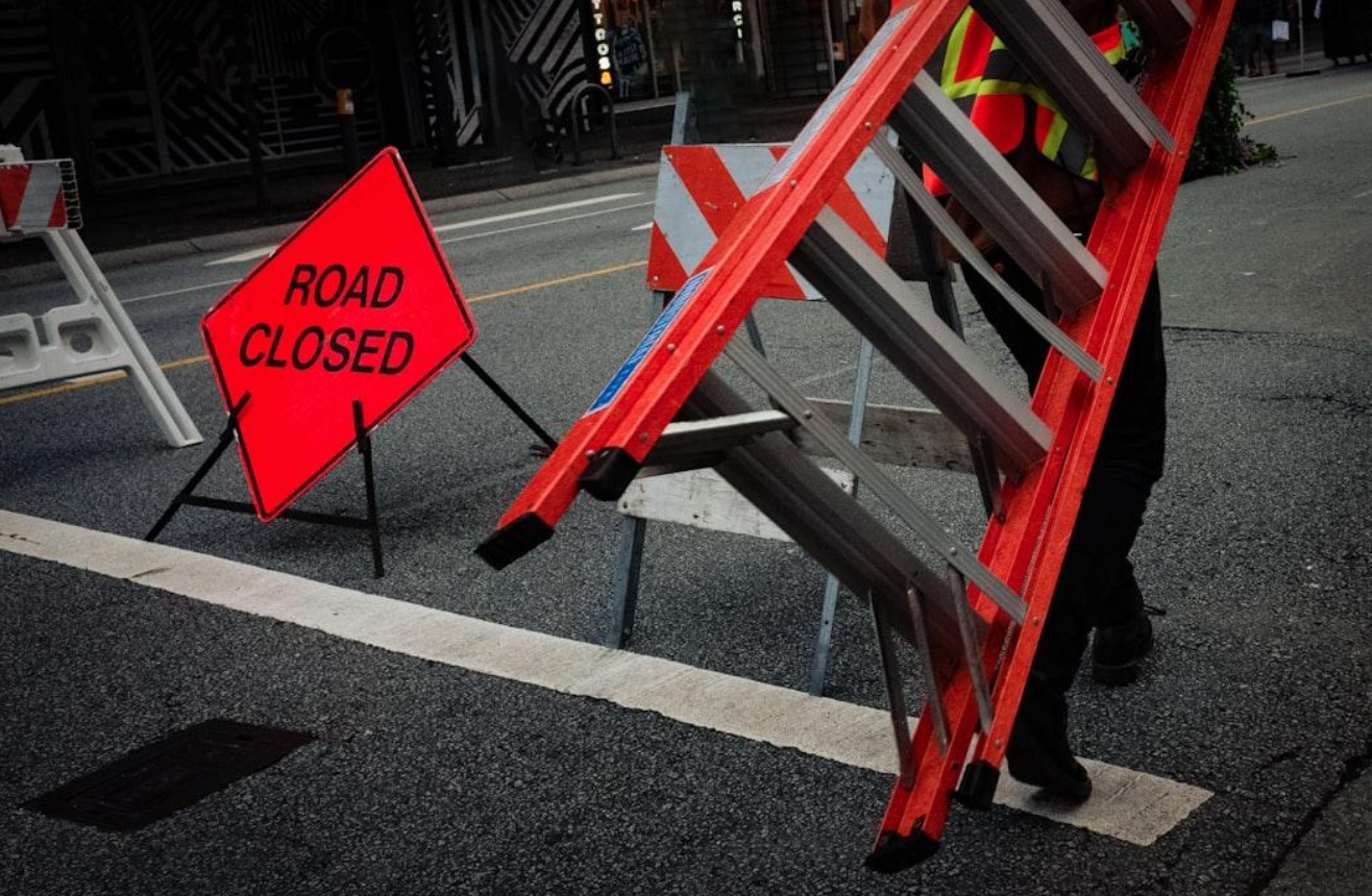 Man carrying ladder next to road closed sign; image by Kingsley Nguyen, via Unsplash.com.