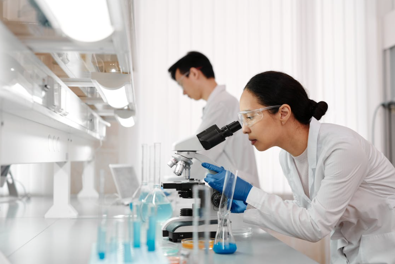 Woman in lab using microscope; image by Edward Jenner, via Pexels.com.