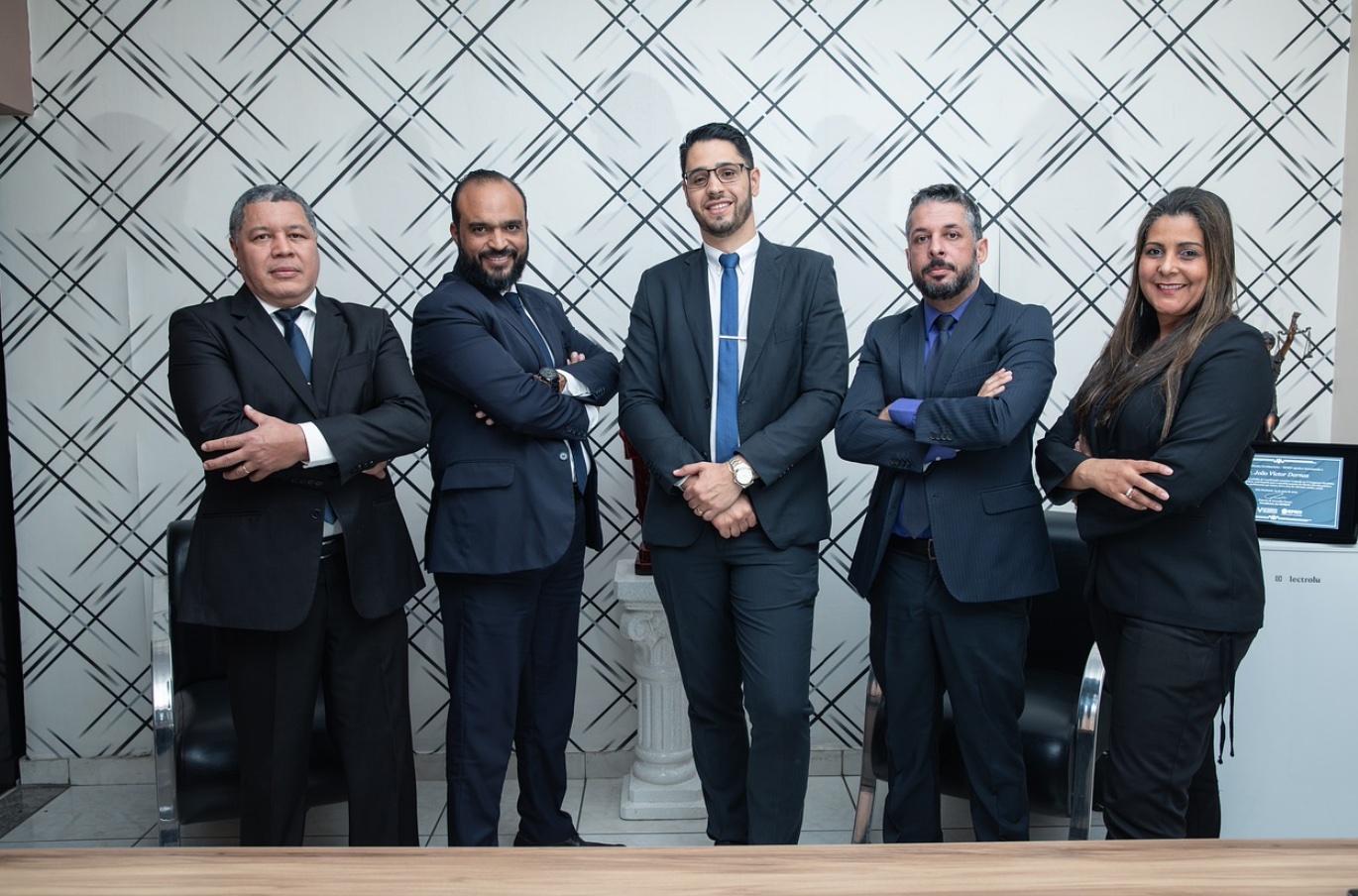 Five lawyers in suits posing in front of crosshatch patterened wallpaper; image by advogadoaguilar, via Pixabay.com.