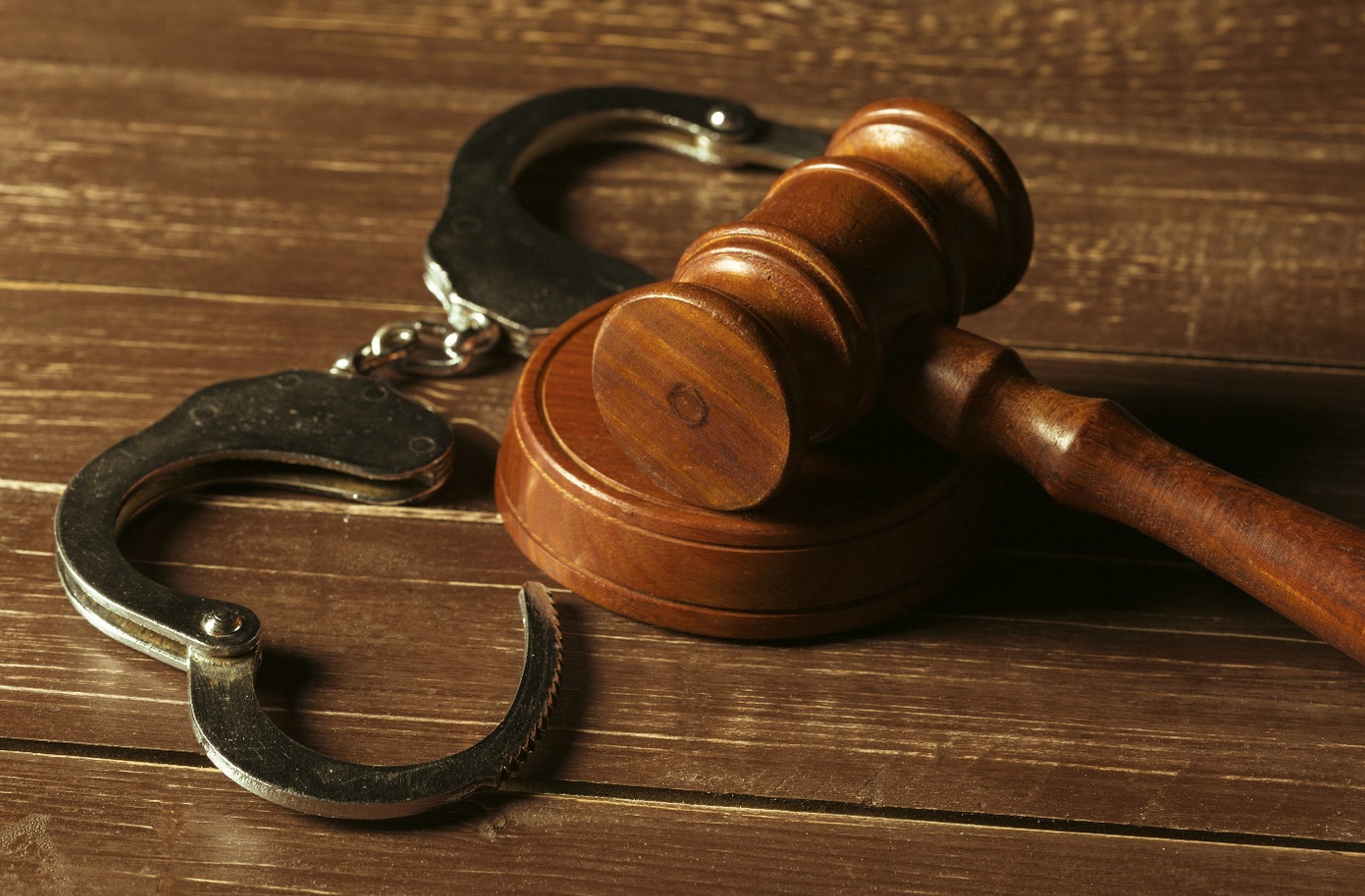 Gavel and open handcuffs on wooden table; image by fabrikasimf, via Freepik.com.