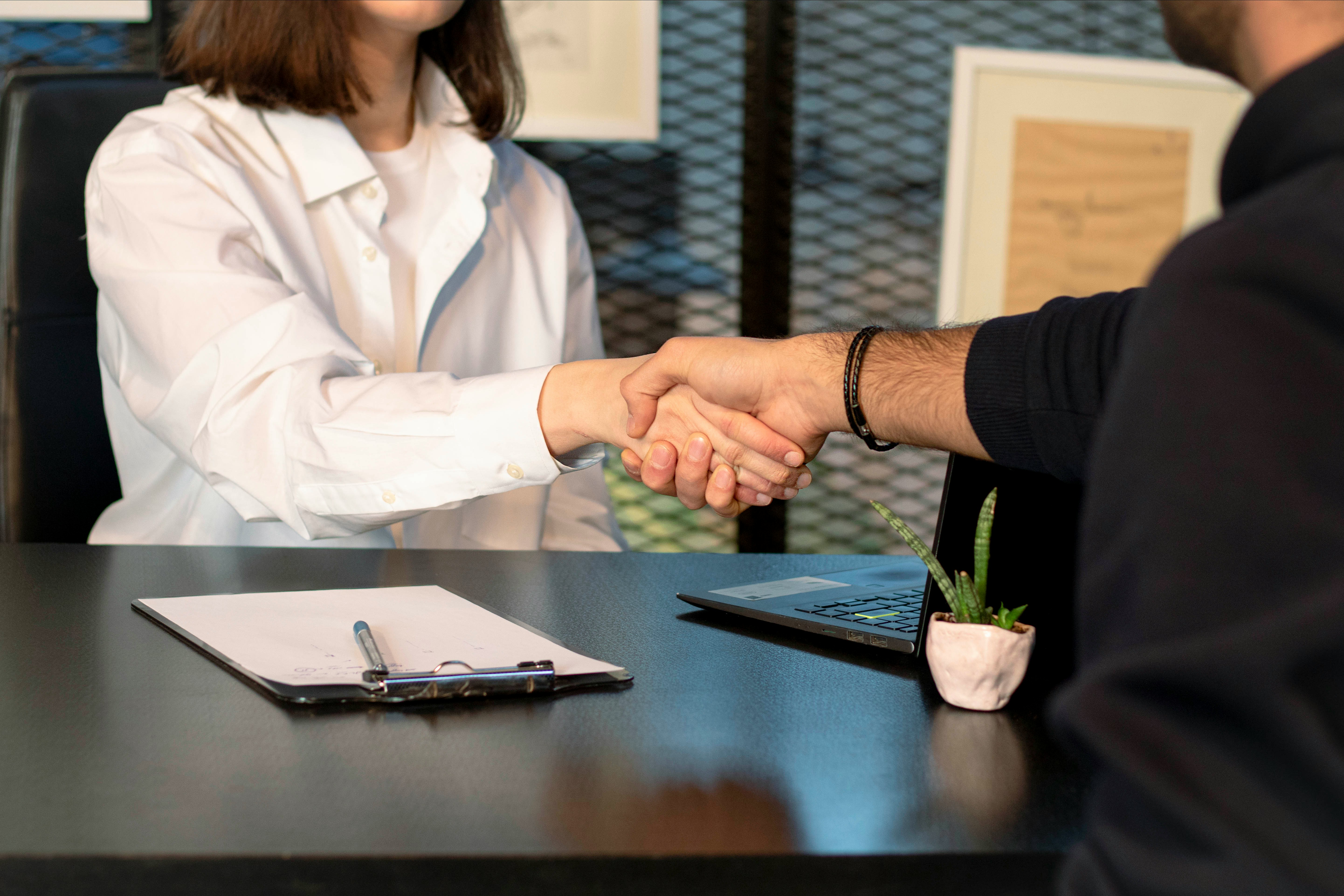 Man and woman shaking hands in front of a laptop; image by Mina Rad, via Unsplash.com.