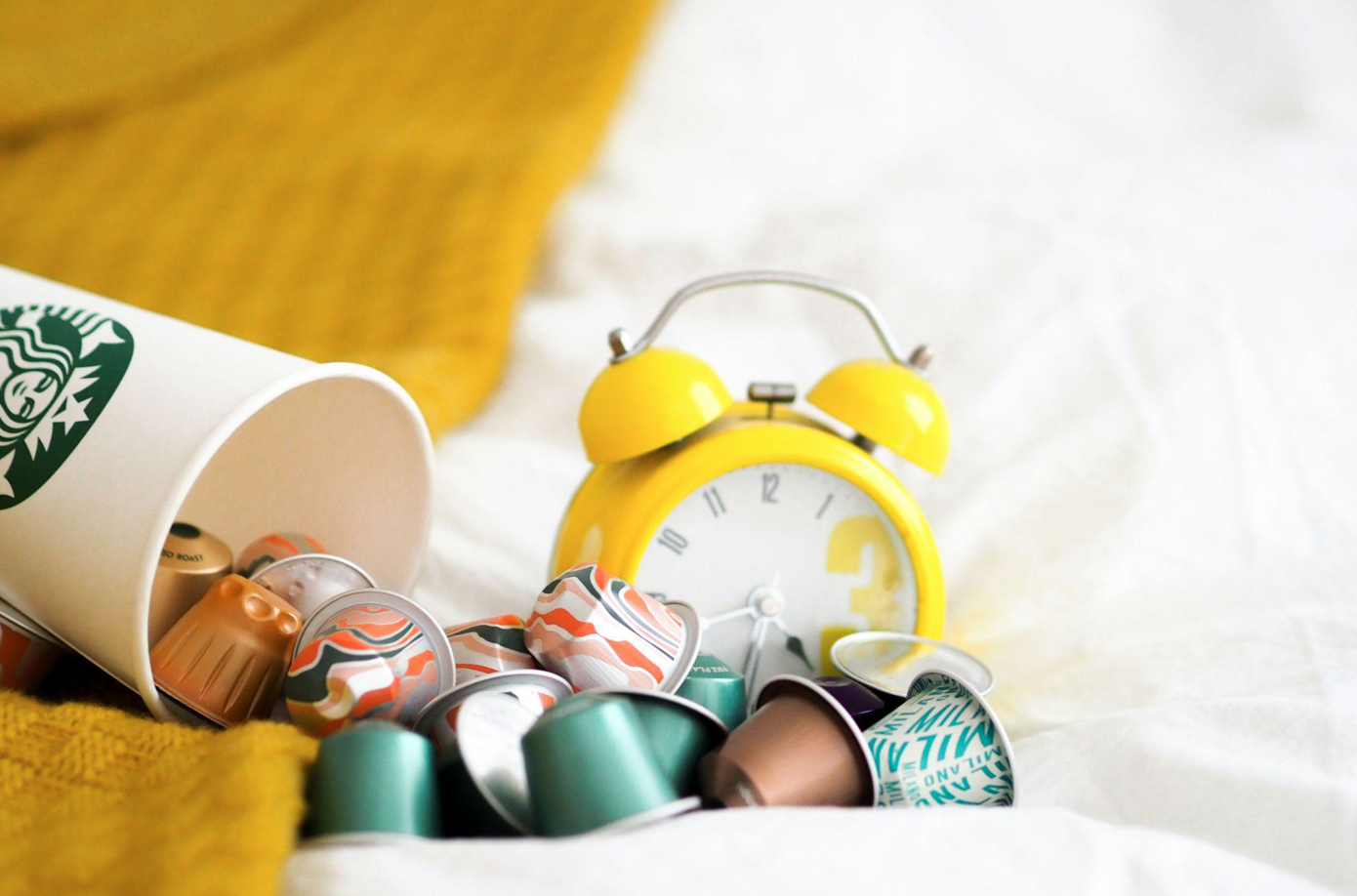 Yellow alarm clock beside green and whit ceramic mugs; image by Laura Chouette, via Unsplash.com.