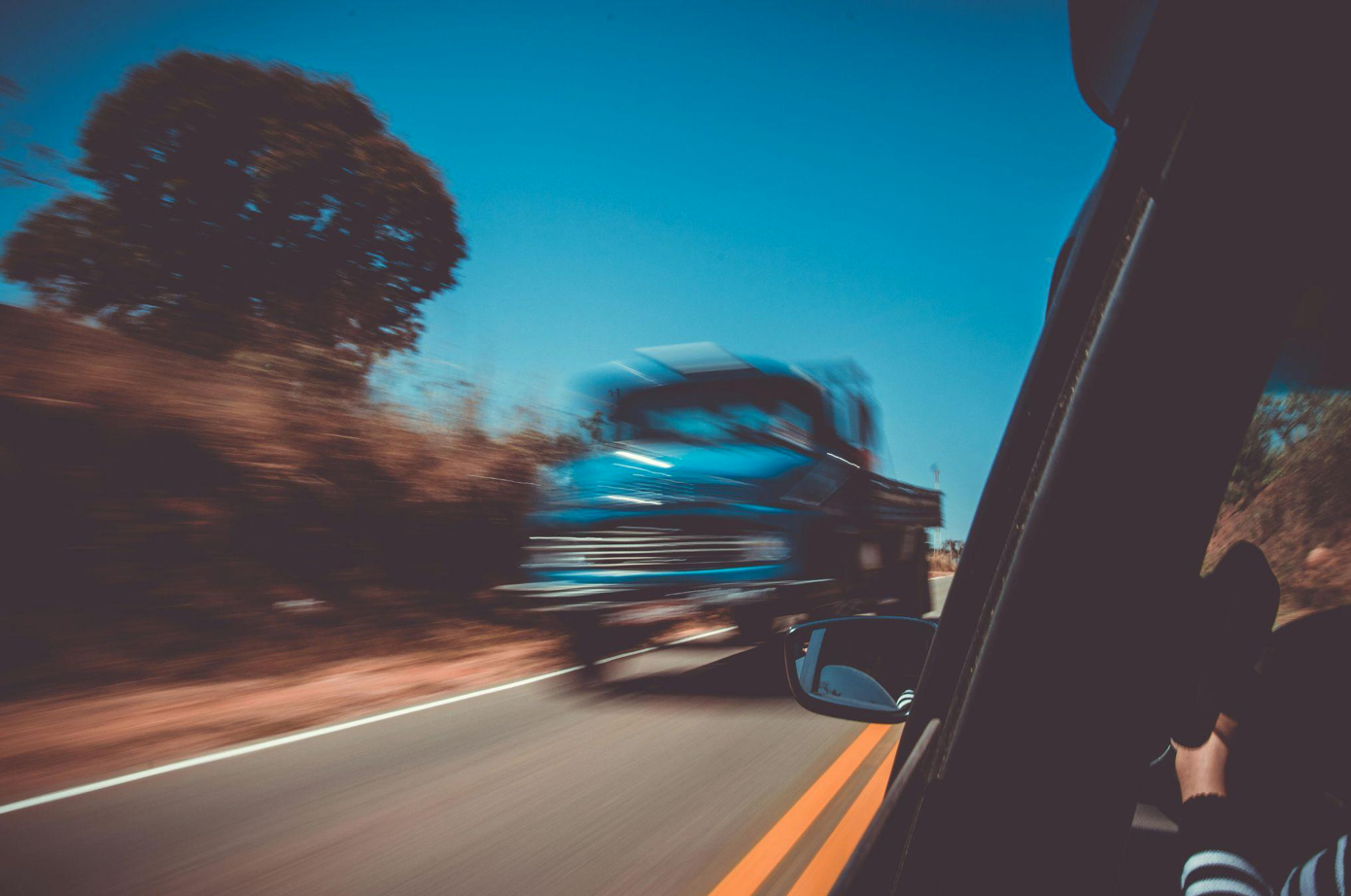 Blue truck passing black car in opposite lane; image by Caio, via Pexels.com.