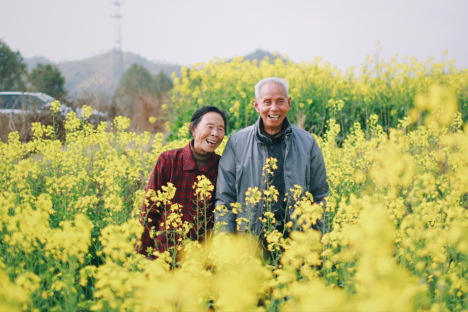 Elderly man and woman in field of yellow flowers; image by Jaddy Liu, via Unsplash.com.