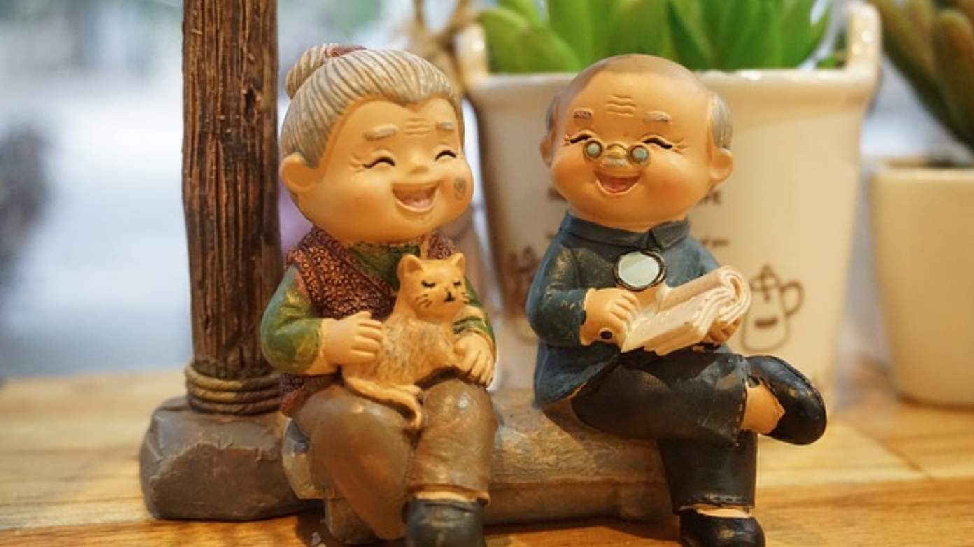 Figurines of an elderly woman and man sitting and chatting; image by FuSuSu, via Pixabay.com.