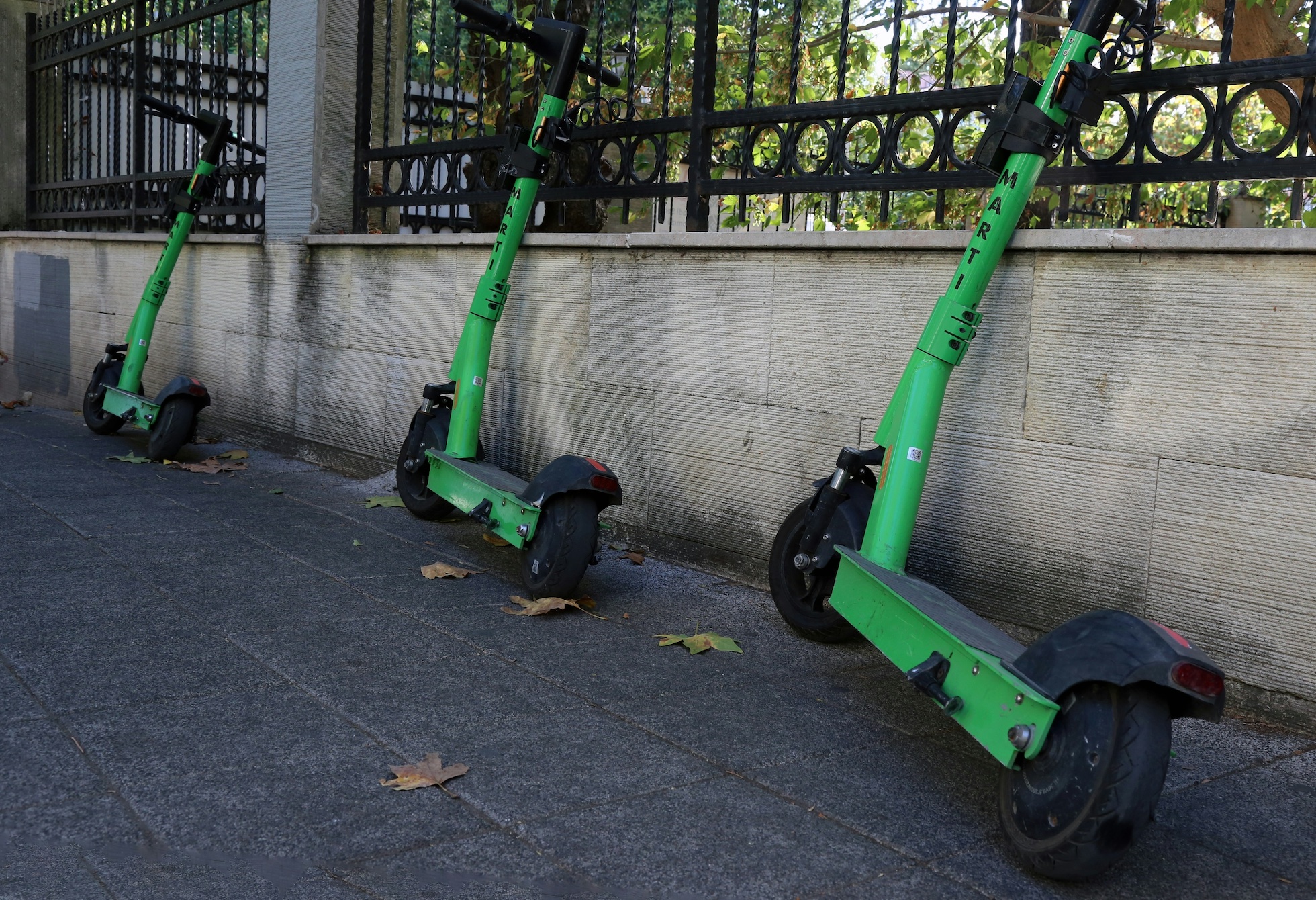 Green e-scooters lined up along a wall; image by Sahin Sezer Dincer, via Unsplash.com.