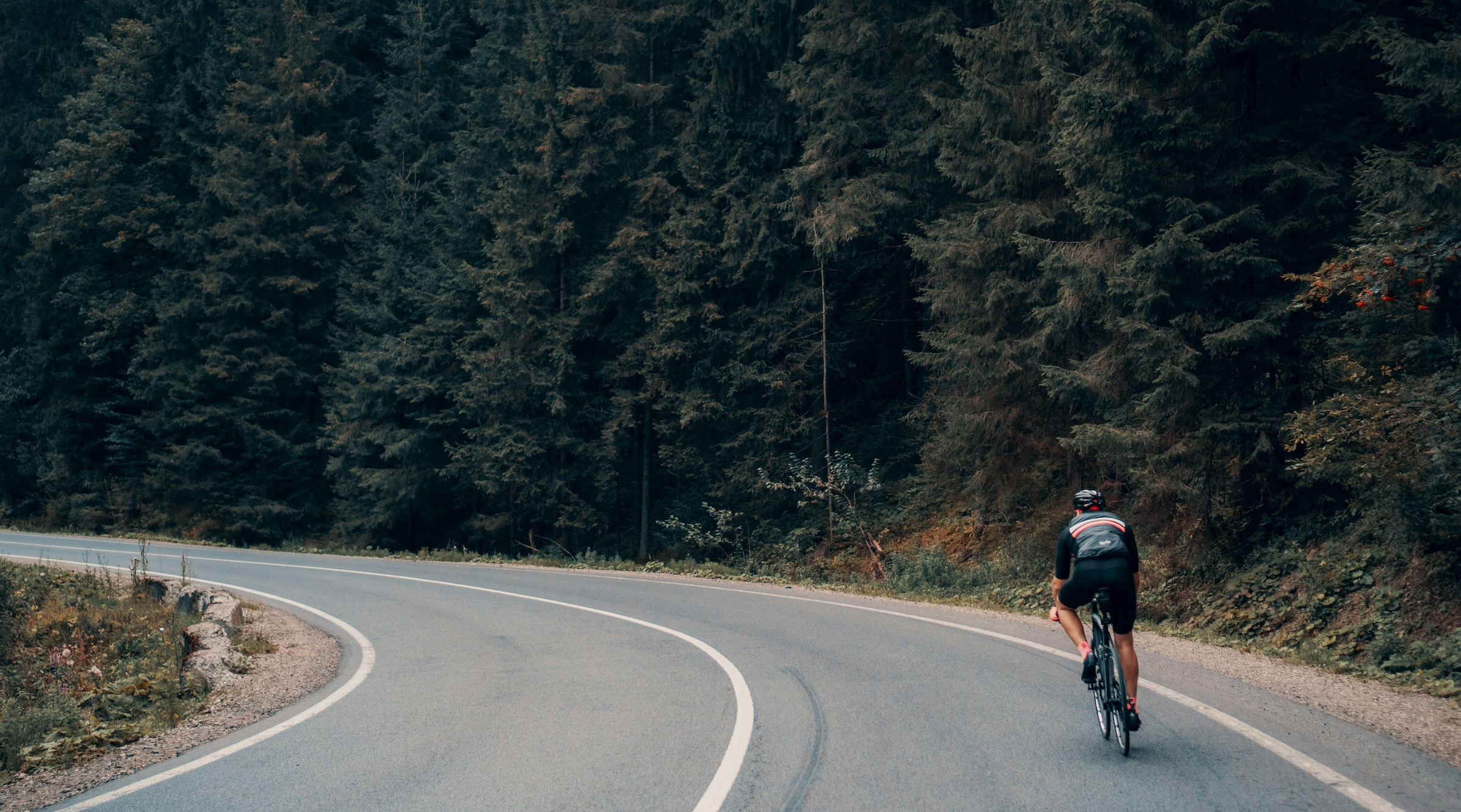 Man riding bike alongside curve in road; image by Viktor Bystrov, via Unsplash.com.