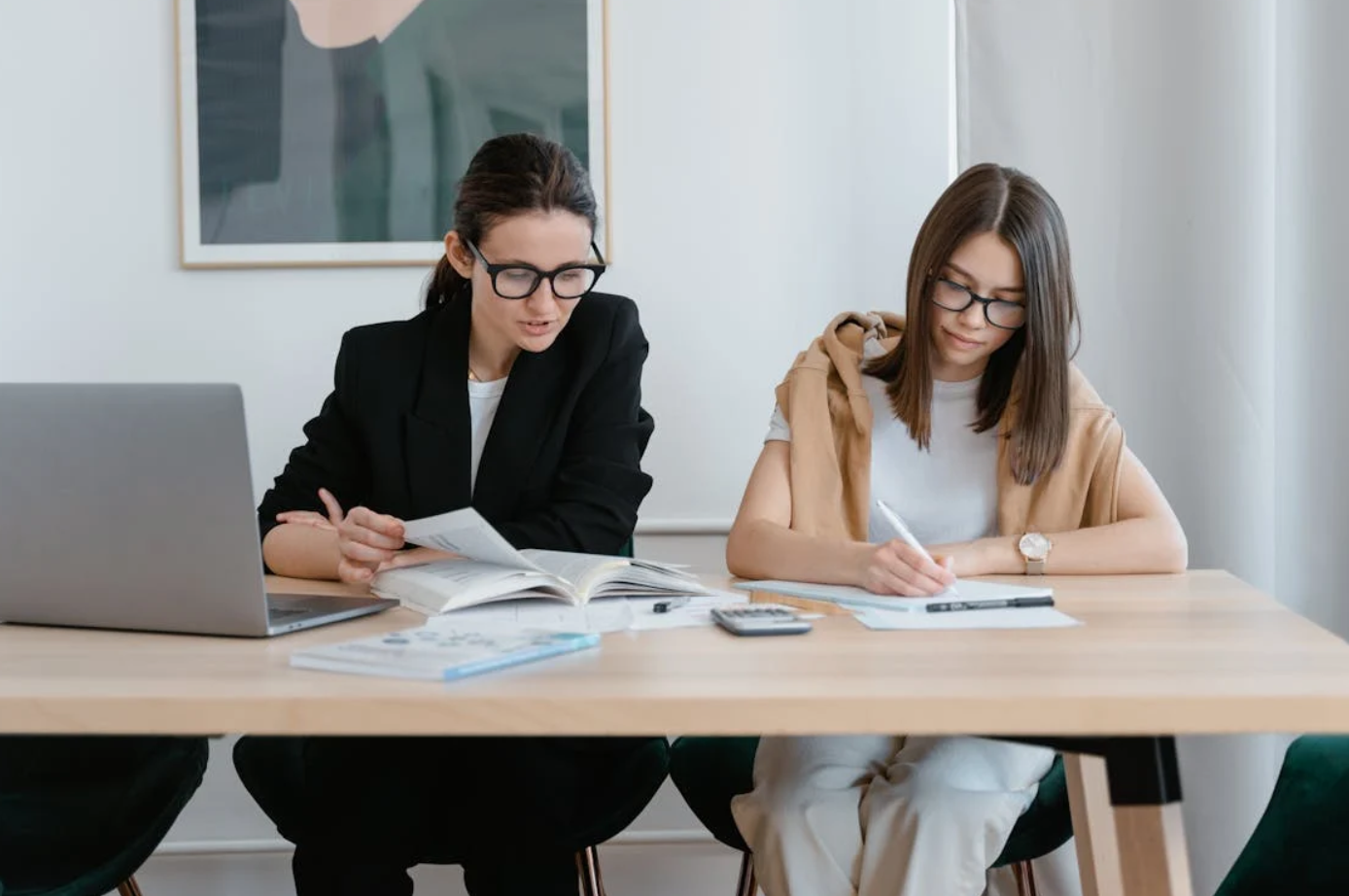 Two women at table writing; image by MART PRODUCTION, via Pexels.com.