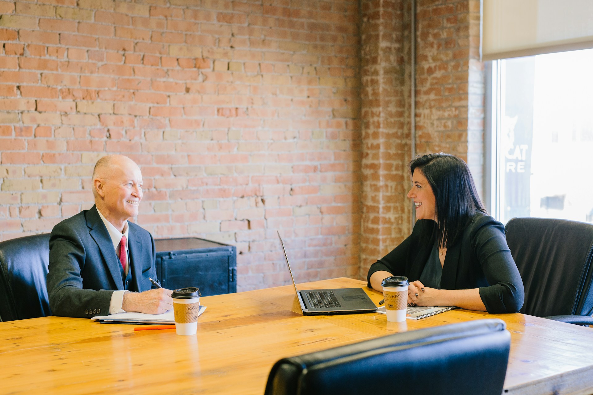 Man and woman at table, man taking notes; image by Amy Hirschi, via Unsplash.com.