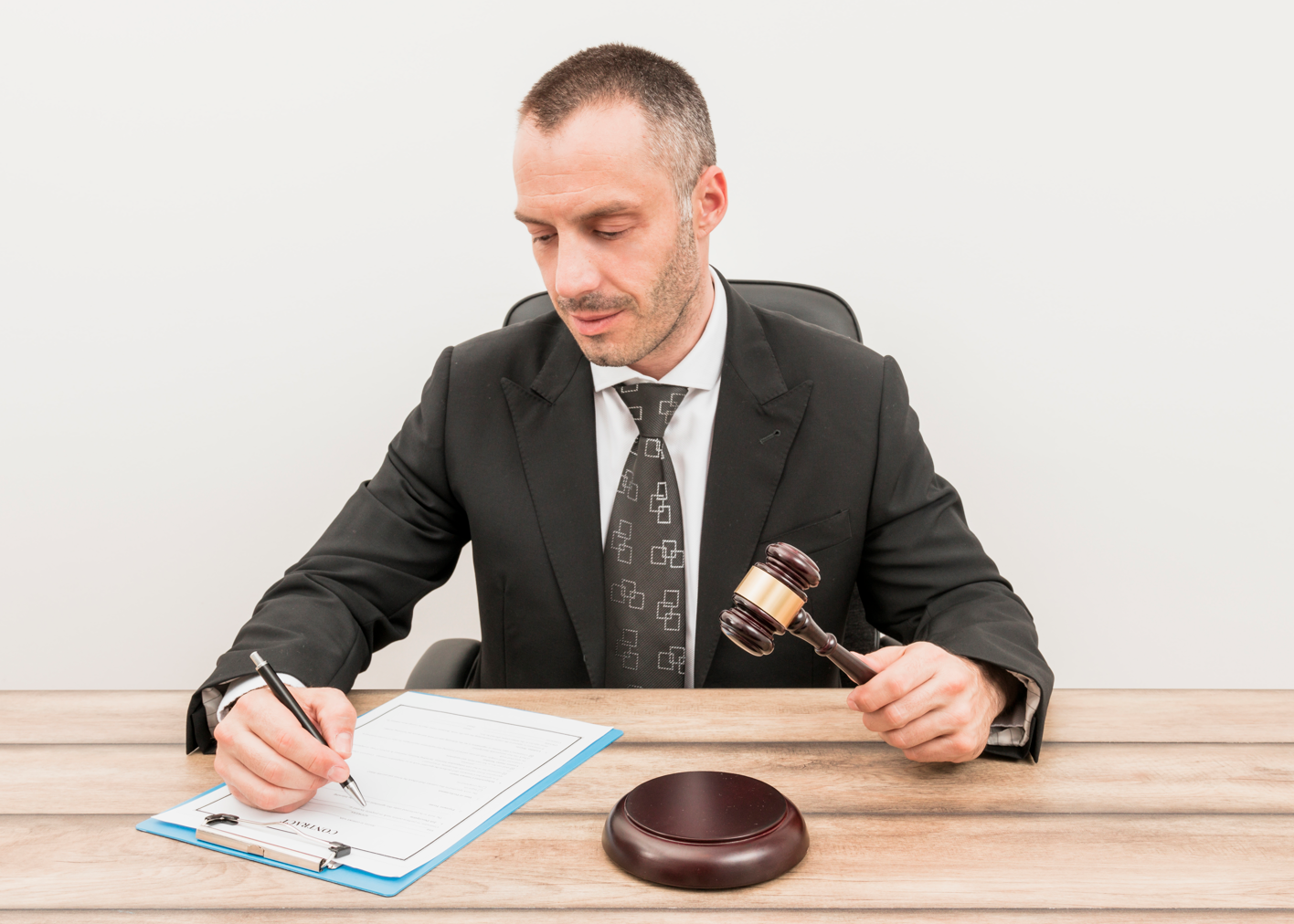 Lawyer filling out form while holding gavel; image by Freepik, via Freepik.com.