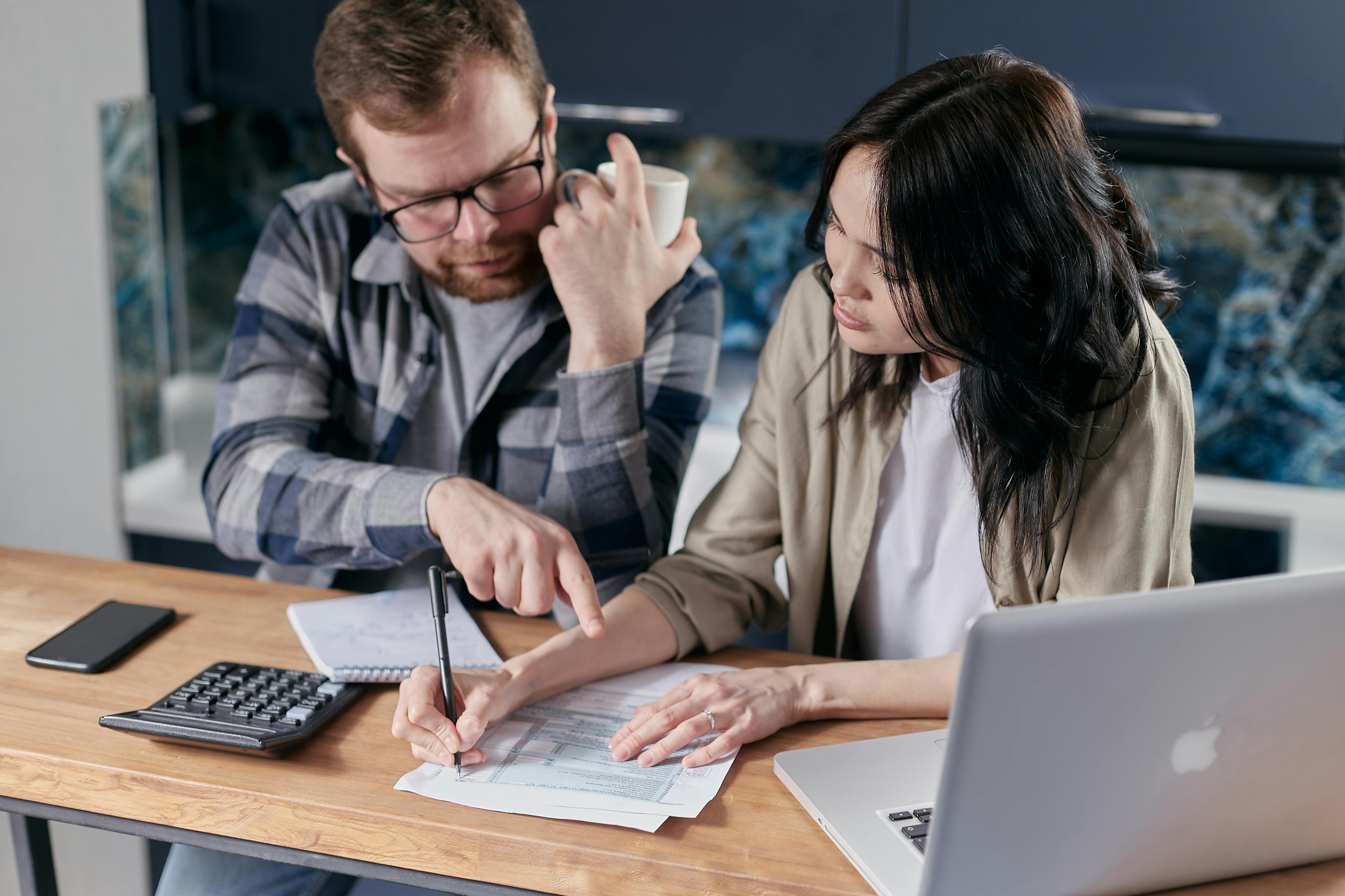 Man and woman with laptop and coffee filling out paperwork; image by Mikhail Nilov, via Pexels.com.