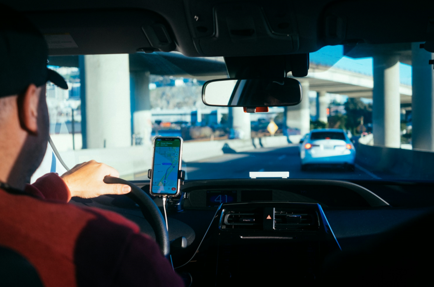 Man driving, iPhone in holder; image by Paul Hanaoka, via Unsplash.com.