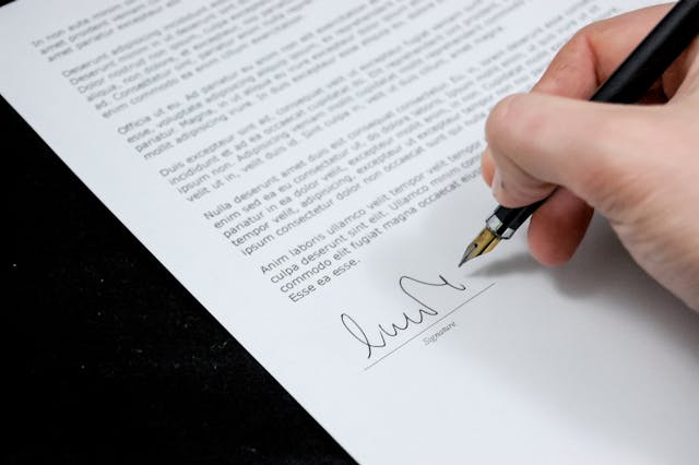 Person signing document; image by Pixabay, via Pexels.com.