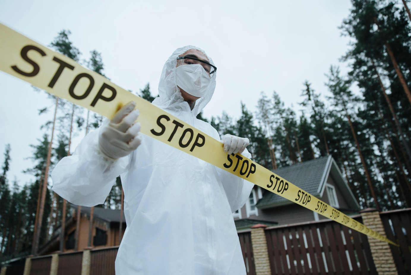 Man in white hazmat suit standing behind crime scene tape; image by cottonbro studio, via Pexels.com.